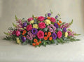 Garden Vibrant casket spray with hot pink roses, purple lisianthus, orange spray roses, yellow carnations and snapdragons
